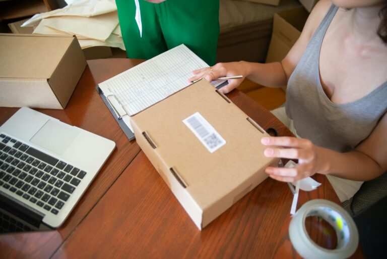 Two people packing online orders in a small business setting with a laptop.